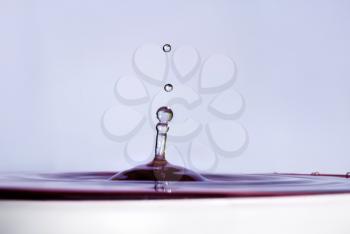 Water drop falling into water and making droplet splash. Shallow depth of field. Selective focus. Lilac shade water.