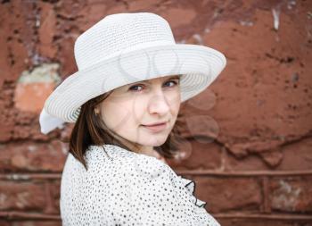 Pretty young woman in a white blouse and hat posing on a background old vintage brown brick wall. Female portrait in a retro style. Selective focus on the model's face.