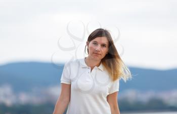 Portrait of a tanned young woman with long hair in white t-shirt. Mountains on blurred background. Shallow depth of field. Focus on model.
