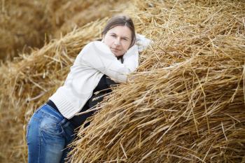Pretty young woman in a white blouse and jeans looking at the camera on a background of straw. Rural scene.
