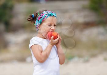Baby girl in a white shirt eats a tasty juicy peach.