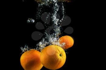 Oranges in water with air bubbles. Wash fruits. Photo on a black background. High speed photography.