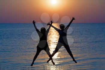 Two girls jumped on the background of the dawn sun. Focus on models. Shallow depth of field.