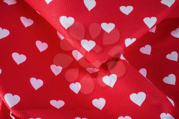 Pattern of white hearts on a bright red fabric with pleats. Top view.