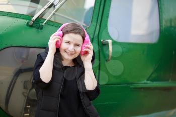 Woman listening to music with fur headphones on the background of helicopter cabin