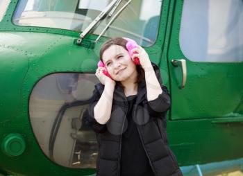 Woman enjoying music in fur headphones on the background of the helicopter