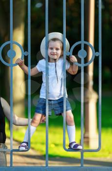 Happy child climbs on the bars of a metal fence. Warm sunny summer day. Vertical shot.