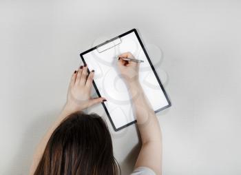 Clipboard with blank paper in female hands. Woman writes on blank white sheet of paper.