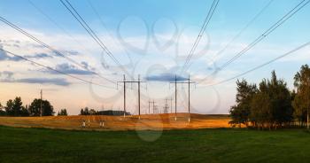 Pillars with high-voltage electric wires over the field after harvest in the countryside. Scenic landscape at sunset. Panoramic shot.