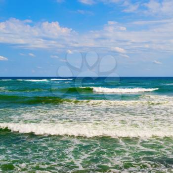 Cloudy blue sky and turquoise surface of the sea with waves.