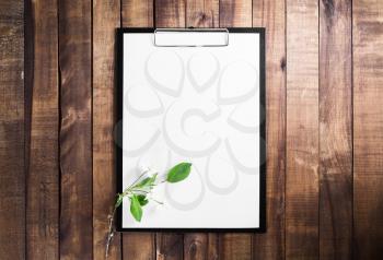 Paper clipboard on vintage wood table background. Blank letterhead and cherry blossoms with green leaves. Responsive design mockup. Top view.