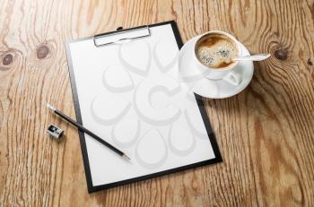 Photo of clipboard with a blank sheet of paper, coffee cup, pencil and sharpener on wooden background with plenty of copy space. Blank template for design presentations and portfolios. Responsive desi