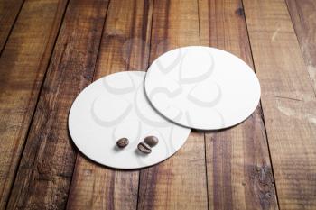 Two blank white coasters and coffee beans on vintage wooden table background.