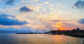 Sunrise on the Black Sea coast. Coastline of the old town Nesebar, Bulgaria. Sun rising on the background of the sky with cumulus clouds. Dawn at the seaside. Silhouettes of houses and boats. Panorami