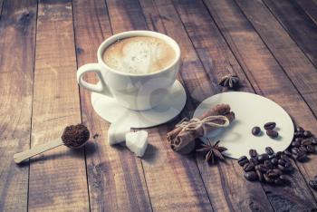 Photo of coffee cup, cinnamon sticks, coffee beans, anise, sugar, spoon and coasters on vintage wood background. Coffee and spices.