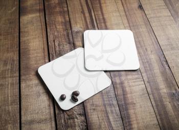 Blank square beer coasters and coffee beans on vintage wooden table background. Responsive design mockup.