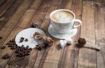 Photo of fresh tasty coffee on wood background. Coffee with spices. Coffee cup with cinnamon sticks, coffee beans, anise, sugar and coasters. Top view.