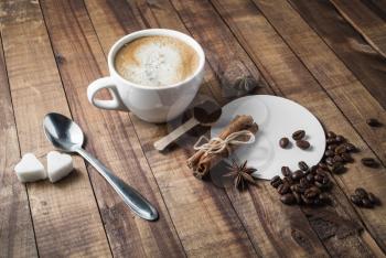 Photo of fresh tasty coffee on old wooden table background. Coffee cup, cinnamon sticks, coffee beans, anise, sugar, spoon and coasters.