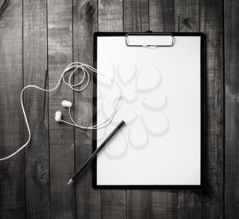 Photo of clipboard with blank letterhead, pencil and headphones on wood table background. Top view.