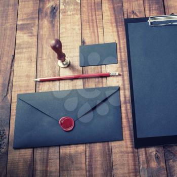 Blank black envelope, business card, pencil, sealing wax and stamp on vintage wooden table background. Blank stationery.