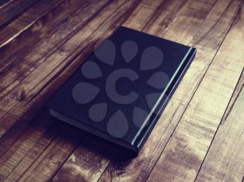 Photo of blank book with black hardcover on wood table background. Vintage toned image.