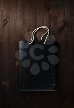 Blank black paper shopping bag with white rope handles on wooden background. Flat lay.