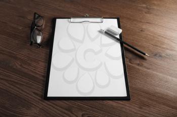 Photo of stationery: clipboard with blank letterhead, pencil, eraser and glasses on wooden background. Responsive design template. Selective focus.
