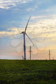 Windmill for electric power production on sunset background. Vertical shot.