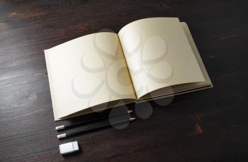 Opened book or booklet with blank kraft paper pages, pencils and eraser on wood table background.