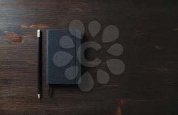 Black notepad and pencil on wood table background. Responsive design template.