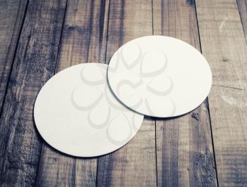 Two blank white beer coasters on vintage wooden table background.