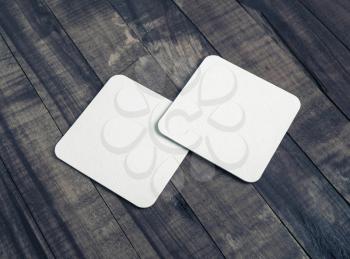 Photo of two blank white square beer coasters on vintage wooden background.