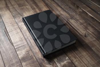 Black book with blank cover mockup on wood table background.