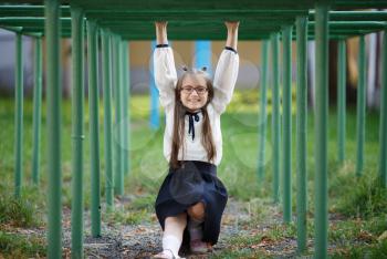 Cheerful child girl hanging on the horizontal bar. Schoolgirl is having fun on the playground. Selective focus.