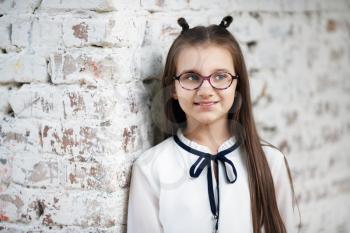 Schoolgirl with glasses. Smiling child girl against white brick wall background. Selective focus.