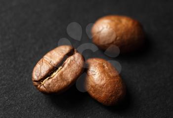 Three roasted coffee beans on black paper background. Shallow depth of field. Selective focus.