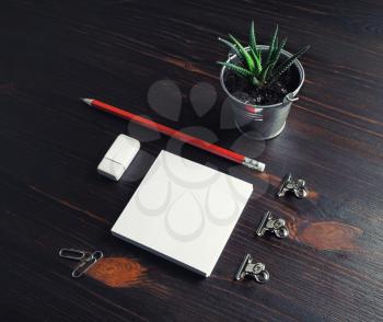 Photo of blank stationery on dark wooden background. Notes, pencil, eraser, and plant.