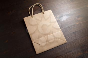 Blank brown paper shopping bag with rope handles on wooden background.