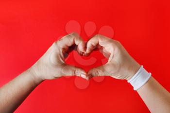 Female hands with white bracelet in the form of heart on red backgroung. Woman hands making heart sign.
