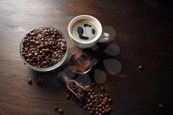 Coffee cup and roasted coffee beans placed on wooden board background.