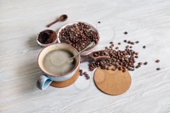 Still life with coffee. Coffee cup, coffee beans, ground powder and beer coaster on light wood kitchen table.