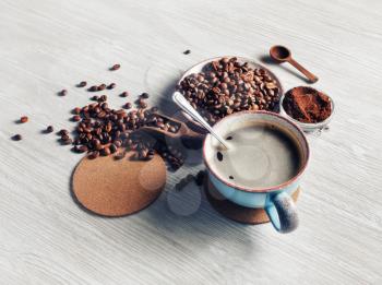 Still life with coffee cup, coffee beans, ground powder and beer coaster on light wooden background.
