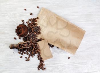 Blank kraft paper coffee package, coffee beans, ground powder and vintage business card on light wooden background. Top view. Flat lay.
