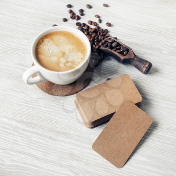 Photo of blank kraft paper business cards, coffee cup, roasted coffee beans on light wood table background. Branding mock up.