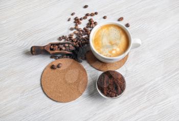 Still life with coffee. Coffee cup, coffee beans, beer coaster and ground powder on light wood table background.