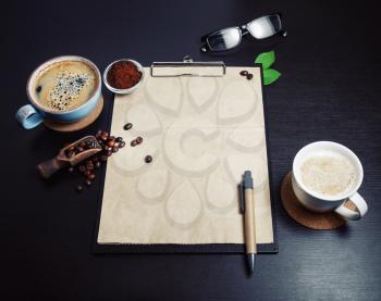 Vintage clipboard, kraft paper letterhead, coffee cups, beans, pen, coffee ground and glasses on black table background. Space for text.