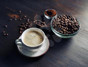 Hot coffee cup with coffee beans roating on wooden table and background.