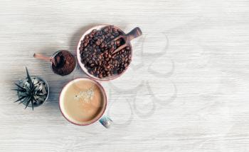 Tasty coffee background. Coffee cup, coffee beans, plant and ground powder on light wood kitchen table. Top view. Flat lay.