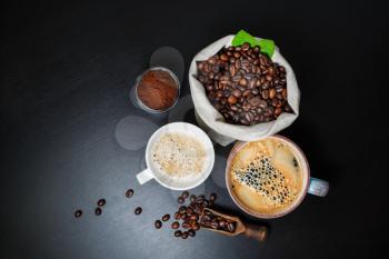 Fresh tasty coffee. Coffee cups, coffee beans and ground powder on black table background. Flat lay.
