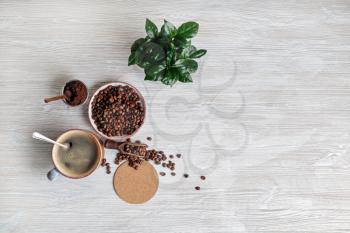 Delicious fresh coffee. Coffee cup, roasted coffee beans, plant, beer coaster and ground powder on light wooden background. Flat lay.